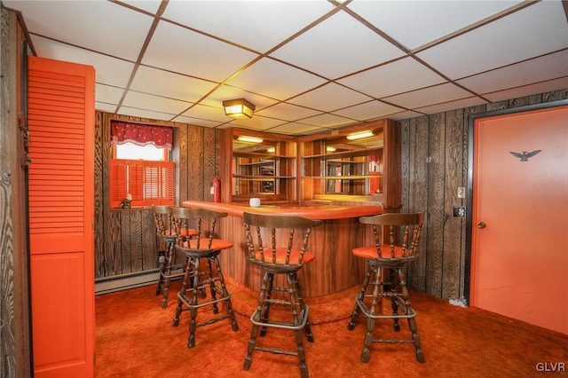 bar with carpet, wooden walls, a baseboard radiator, and a paneled ceiling