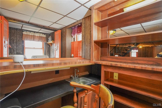 interior space featuring a drop ceiling, wooden walls, and sink