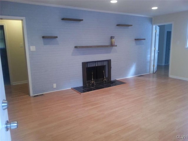 unfurnished living room with a tiled fireplace, hardwood / wood-style flooring, and crown molding