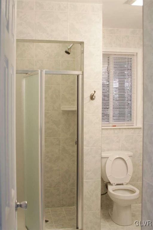 bathroom with tile walls, toilet, and a shower with door