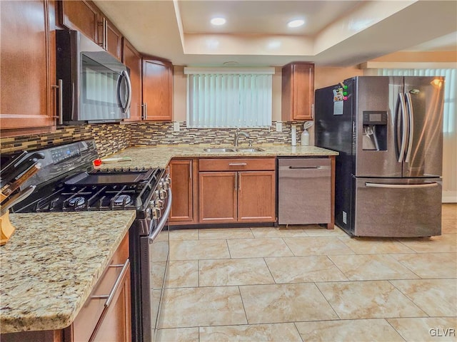 kitchen with a raised ceiling, sink, light stone counters, stainless steel appliances, and backsplash