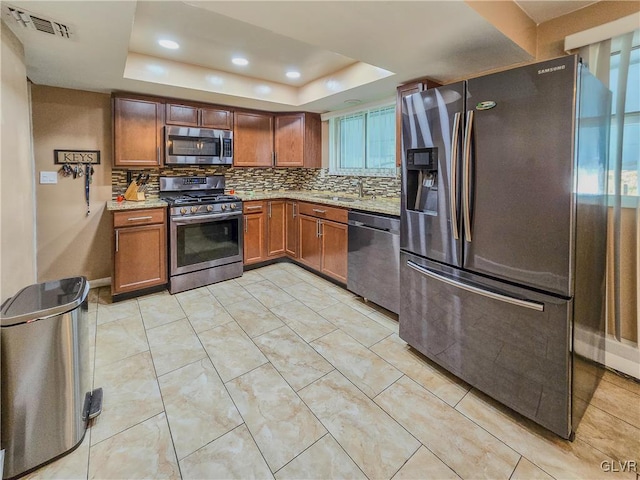 kitchen with light stone counters, decorative backsplash, stainless steel appliances, a raised ceiling, and sink