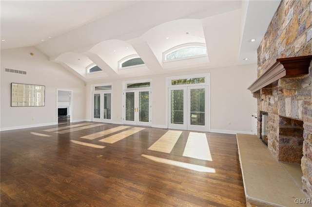 unfurnished living room featuring french doors, a stone fireplace, dark wood-type flooring, and high vaulted ceiling