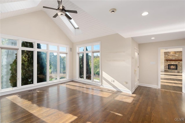 interior space with high vaulted ceiling, ceiling fan, a stone fireplace, dark hardwood / wood-style flooring, and a skylight