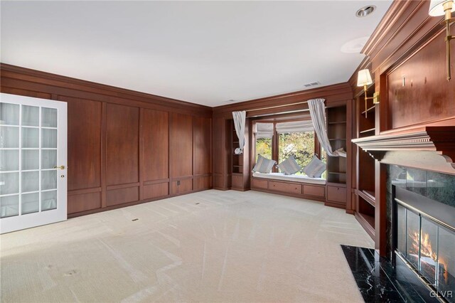 unfurnished living room featuring a fireplace, wood walls, crown molding, and light colored carpet