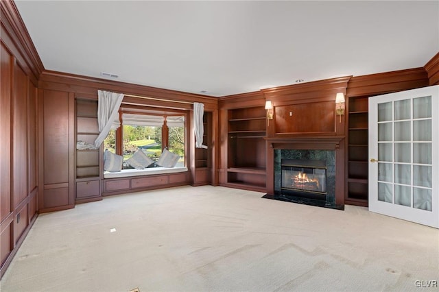 unfurnished living room featuring wood walls, built in features, crown molding, light carpet, and a high end fireplace