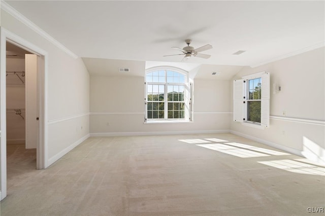 empty room featuring light colored carpet, vaulted ceiling, ornamental molding, and a wealth of natural light