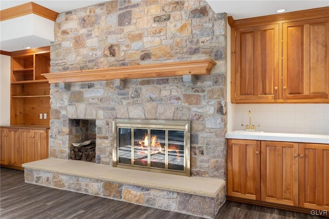 unfurnished living room featuring sink, dark wood-type flooring, and a stone fireplace