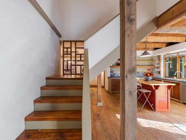 staircase featuring sink, beamed ceiling, and wood-type flooring