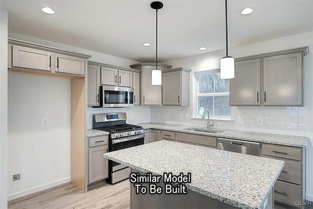 kitchen with light wood-type flooring, decorative light fixtures, sink, appliances with stainless steel finishes, and a center island