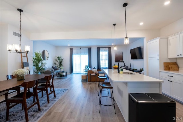 kitchen with white cabinets, an island with sink, hanging light fixtures, sink, and light wood-type flooring