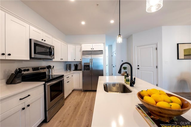 kitchen featuring light wood-type flooring, pendant lighting, sink, white cabinets, and appliances with stainless steel finishes