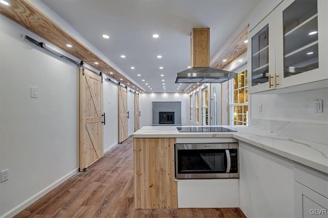 kitchen with a barn door, island exhaust hood, stainless steel appliances, light stone countertops, and hardwood / wood-style flooring