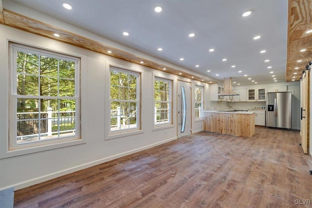 kitchen with white cabinets, kitchen peninsula, extractor fan, stainless steel fridge with ice dispenser, and light wood-type flooring