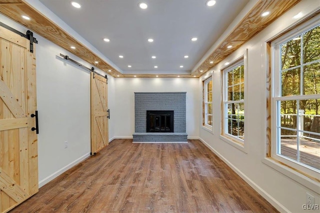 unfurnished living room with hardwood / wood-style flooring, a brick fireplace, and a barn door