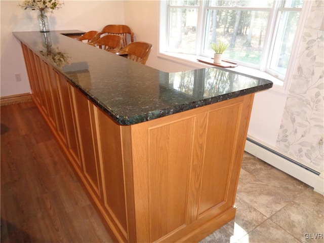 bar featuring baseboard heating, dark stone countertops, and light hardwood / wood-style flooring