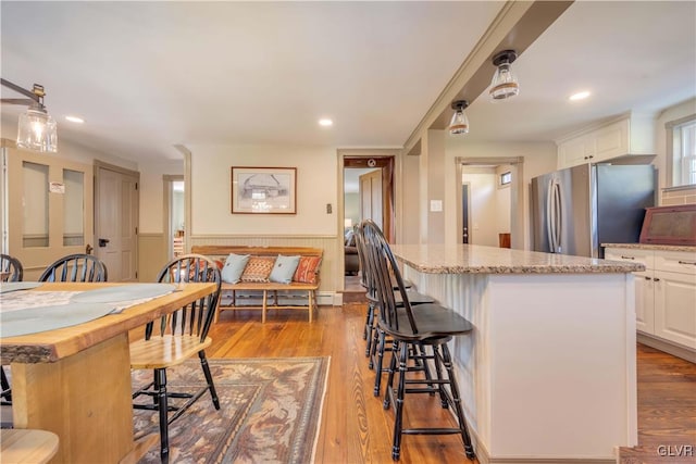 kitchen featuring a kitchen island, stainless steel refrigerator, white cabinetry, and light wood-type flooring