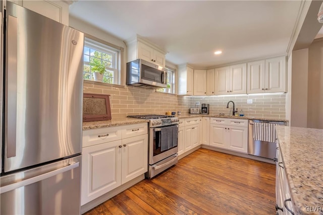 kitchen with light stone counters, white cabinetry, light hardwood / wood-style flooring, appliances with stainless steel finishes, and backsplash