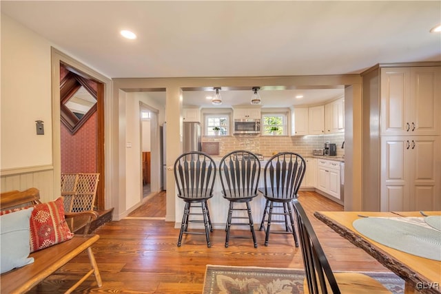 kitchen with wood-type flooring, backsplash, white cabinets, and a breakfast bar