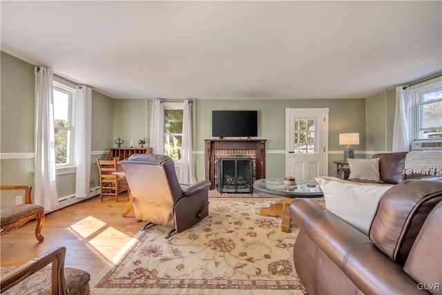 living room with a brick fireplace, light wood-type flooring, and a baseboard heating unit