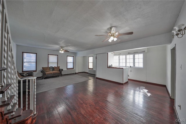 unfurnished living room featuring ceiling fan, a textured ceiling, dark hardwood / wood-style floors, and a healthy amount of sunlight