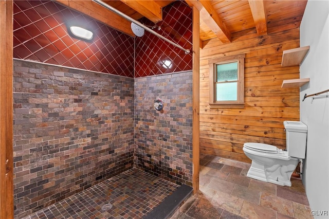 bathroom featuring beamed ceiling, a tile shower, wood walls, and toilet