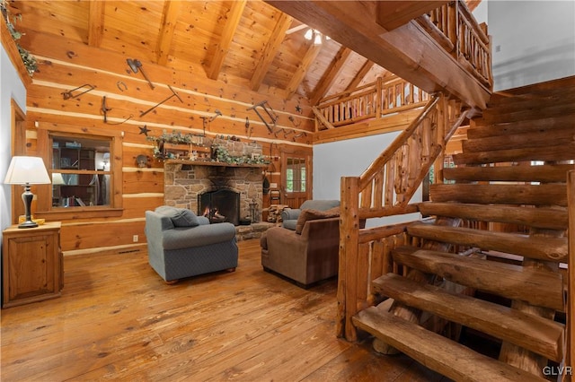 living room with beamed ceiling, wood ceiling, a stone fireplace, high vaulted ceiling, and light wood-type flooring