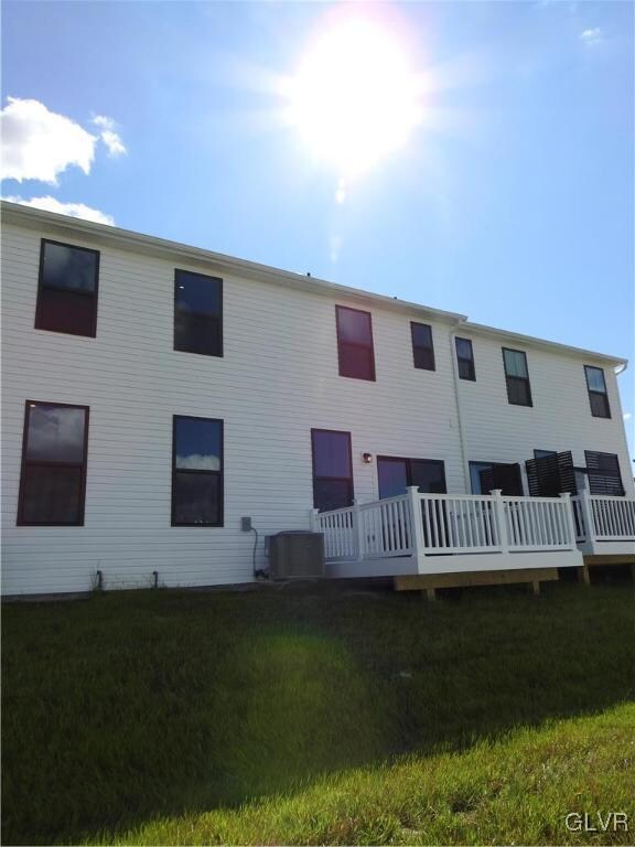 rear view of house featuring cooling unit, a deck, and a lawn