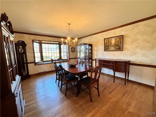 dining space with hardwood / wood-style flooring, crown molding, and an inviting chandelier