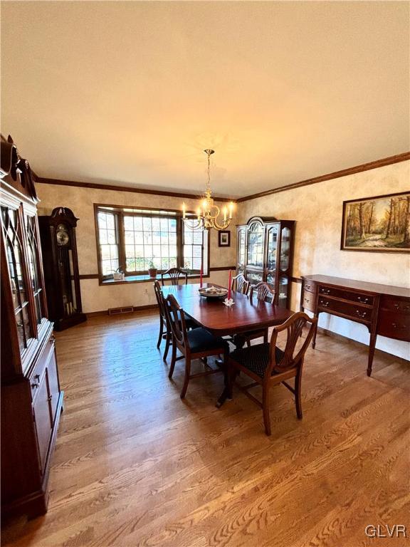 dining area featuring crown molding, wood-type flooring, and a notable chandelier