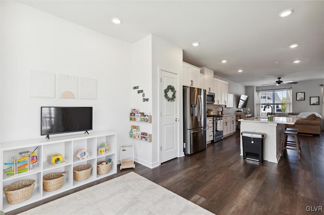 kitchen with appliances with stainless steel finishes, a breakfast bar, a kitchen island with sink, dark wood-type flooring, and white cabinets