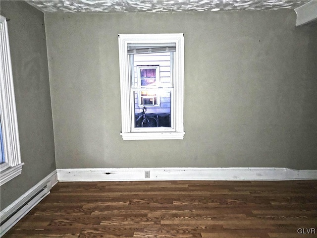 unfurnished room featuring dark hardwood / wood-style floors and a baseboard heating unit