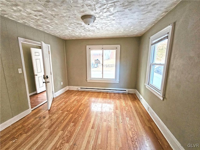 unfurnished room featuring a healthy amount of sunlight, a baseboard radiator, and light wood-type flooring