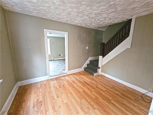 unfurnished room featuring wood walls, a baseboard radiator, and light hardwood / wood-style flooring