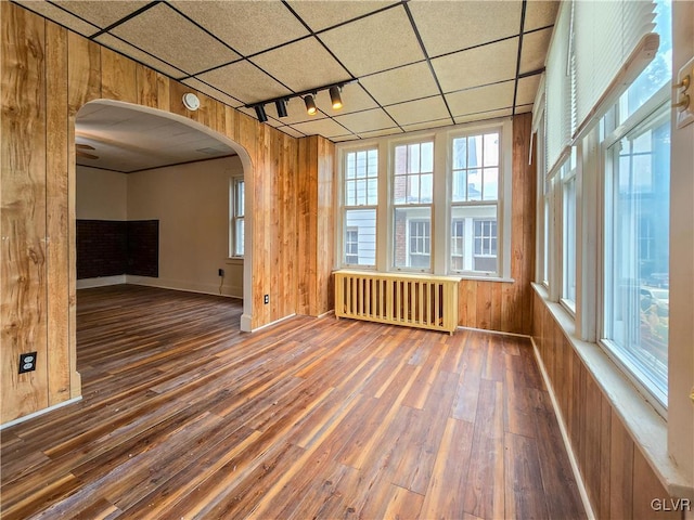 empty room with track lighting, dark hardwood / wood-style floors, radiator heating unit, and wood walls