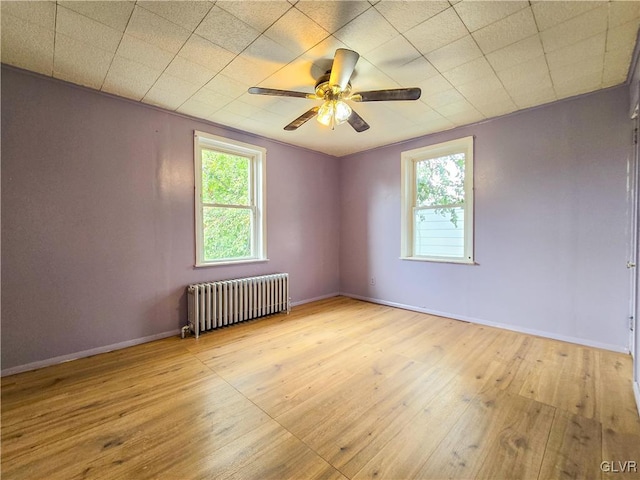 spare room featuring radiator heating unit, light wood-type flooring, and ceiling fan