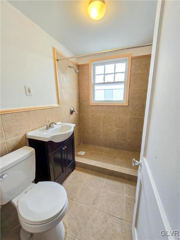 bathroom featuring vanity, toilet, tile walls, and tiled shower