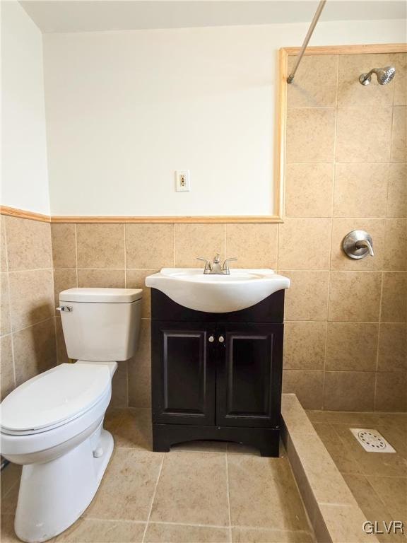 bathroom with a tile shower, tile walls, toilet, vanity, and tile patterned floors