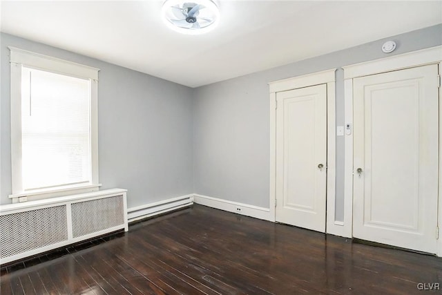 unfurnished room with dark hardwood / wood-style flooring, radiator heating unit, and baseboard heating