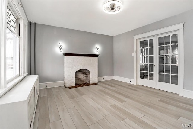 unfurnished living room featuring a brick fireplace, light hardwood / wood-style floors, ceiling fan, and french doors