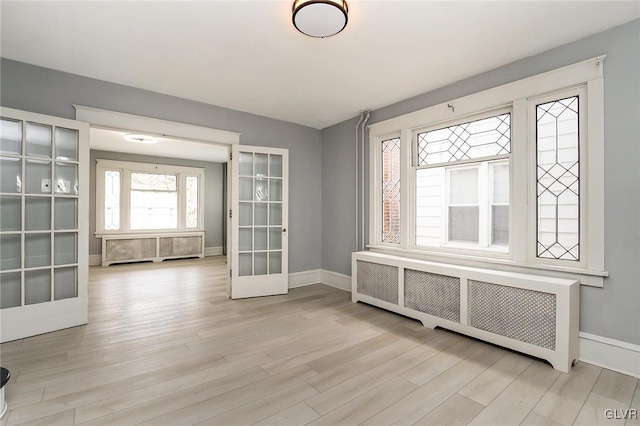 interior space with radiator heating unit, light wood-type flooring, and french doors