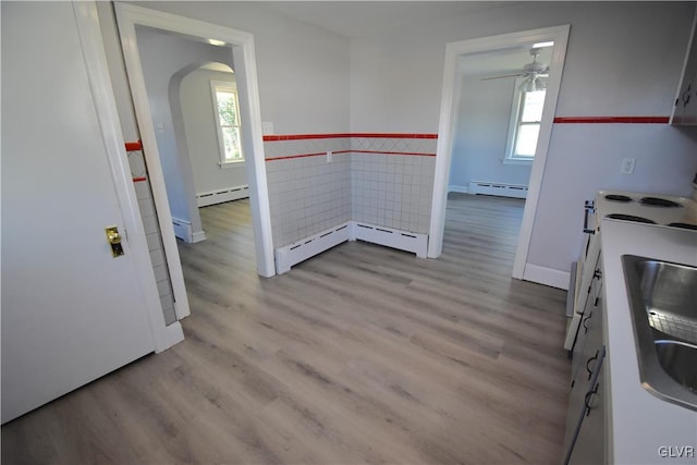 unfurnished dining area featuring a baseboard radiator, light hardwood / wood-style flooring, and a healthy amount of sunlight