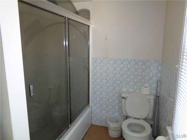 bathroom with tile walls, combined bath / shower with glass door, and toilet