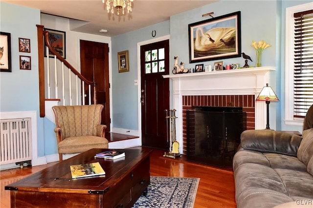 living room featuring radiator, wood-type flooring, plenty of natural light, and a brick fireplace