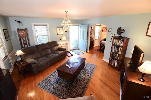 living room featuring radiator heating unit, light wood-type flooring, and an inviting chandelier