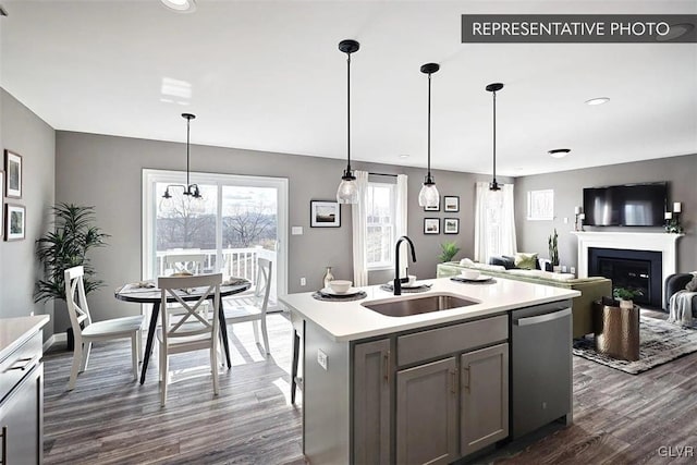 kitchen featuring stainless steel dishwasher, a center island with sink, sink, and hanging light fixtures