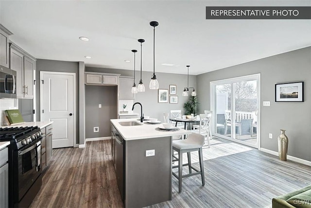 kitchen featuring an island with sink, stainless steel appliances, decorative light fixtures, gray cabinets, and dark hardwood / wood-style flooring