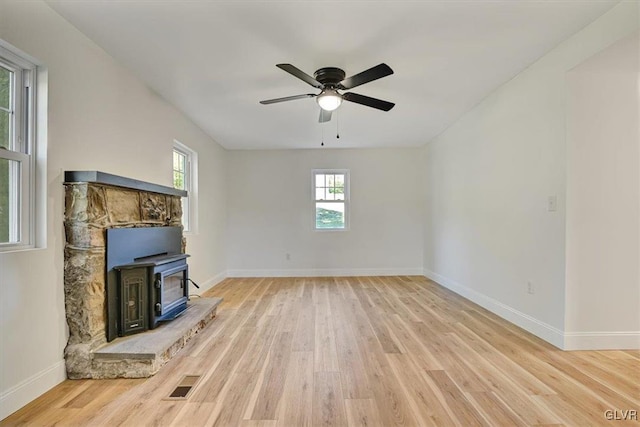 unfurnished living room featuring light wood-type flooring, a wood stove, and ceiling fan