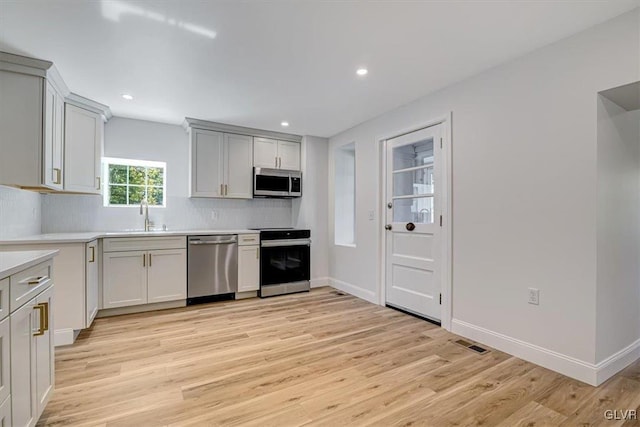 kitchen featuring white cabinetry, sink, stainless steel appliances, light hardwood / wood-style flooring, and backsplash