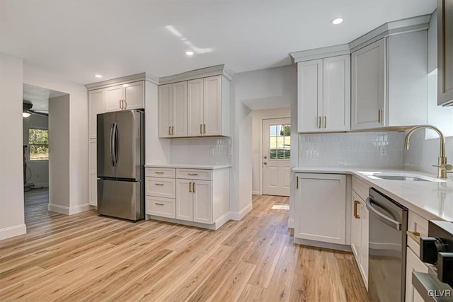 kitchen featuring backsplash, stainless steel appliances, ceiling fan, sink, and light hardwood / wood-style flooring